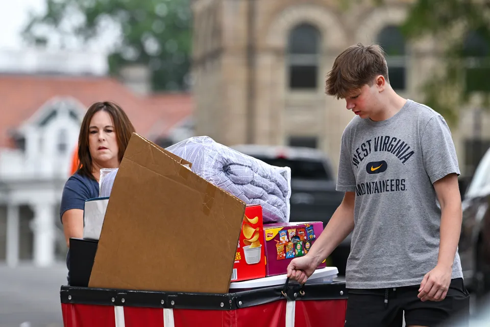 Woman, young man push wheeled tote loaded with dorm supplies. 