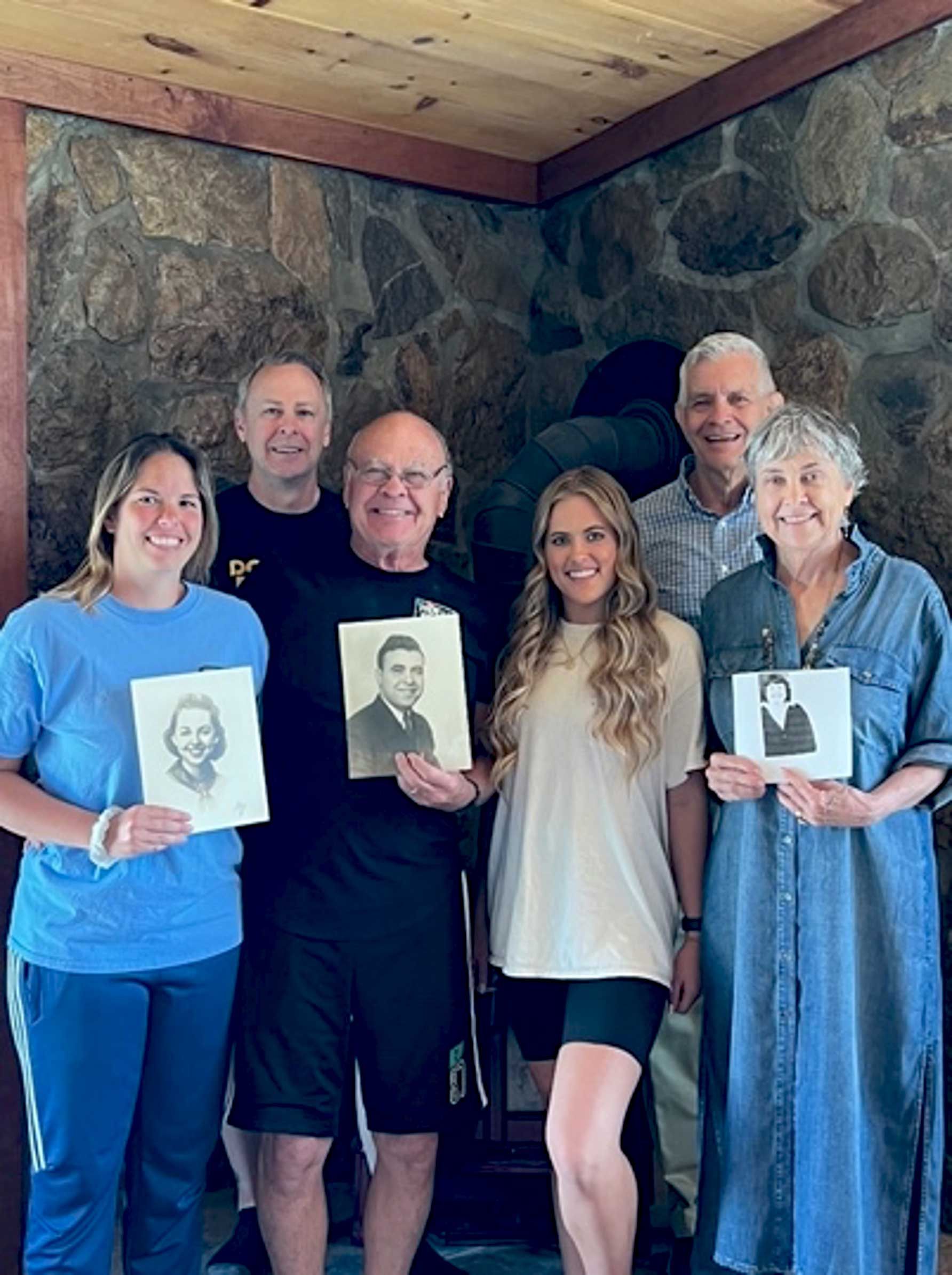 five family members smile for the camera while holding black and white photos of relatives