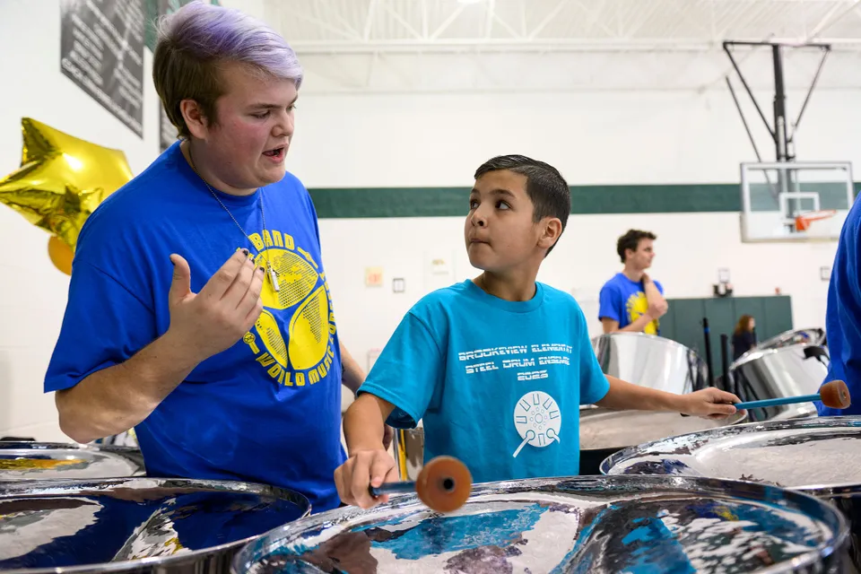 an older student talks as a younger student plays steel drums
