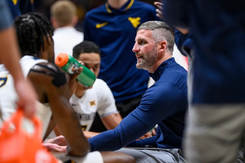 West Virginia interim coach Josh Eilert is surrounded by players while sitting during a time out.