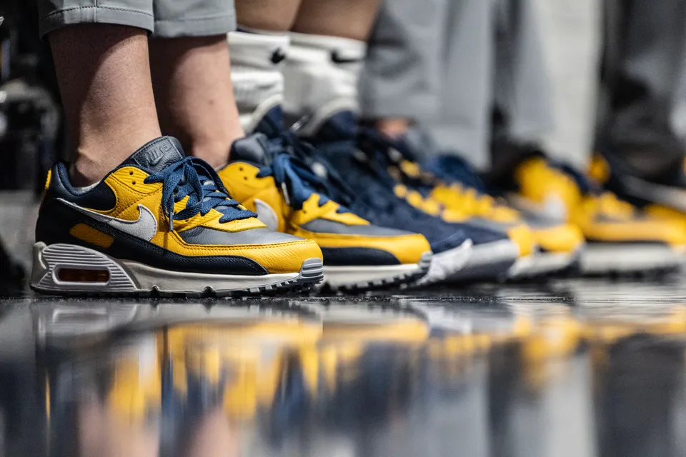Matching gold and blue Nike Air Max shoes reflect on the basketball court sidelines.