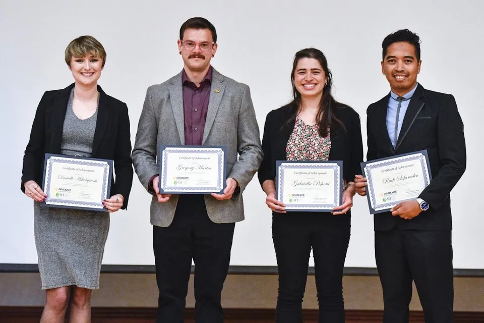 Four graduate students smiling with their awards