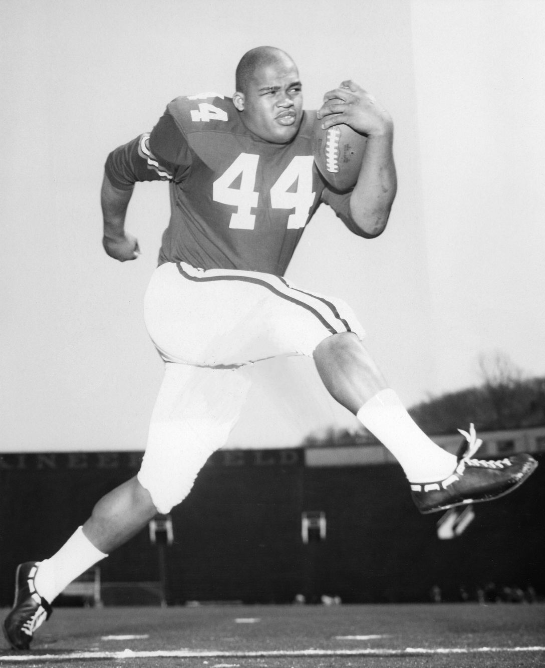 Jim Braxton, wearing a No. 44 jersey, poses as if running while carrying a football.